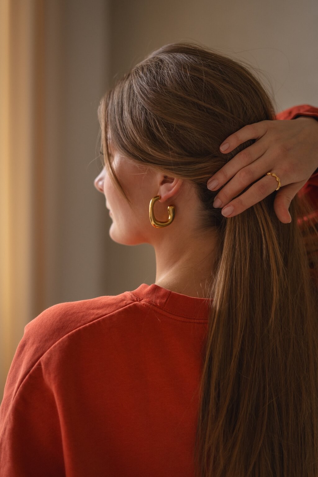 Model trägt 18 Karat goldene Ohrringe von AGVA Studio, die das Gesicht elegant umrahmen und einen goldenen Ring von AGVA Studio am Finger.
